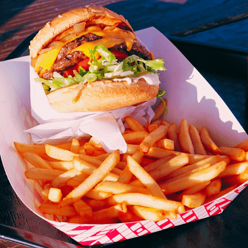 Cheeseburger with lettuce and tomato, side of fries in a paper tray.