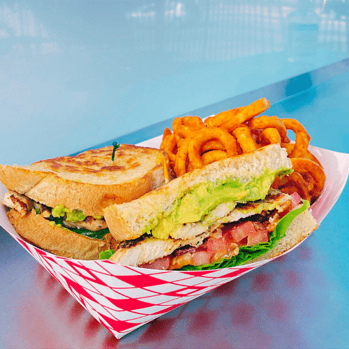 Grilled chicken sandwich with avocado and curly fries.