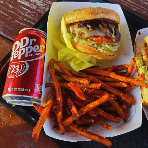A burger with sides of sweet potato fries and a can of Dr Pepper.
