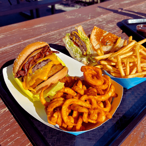 Cheeseburger with fries and onion rings on a sunny outdoor table.