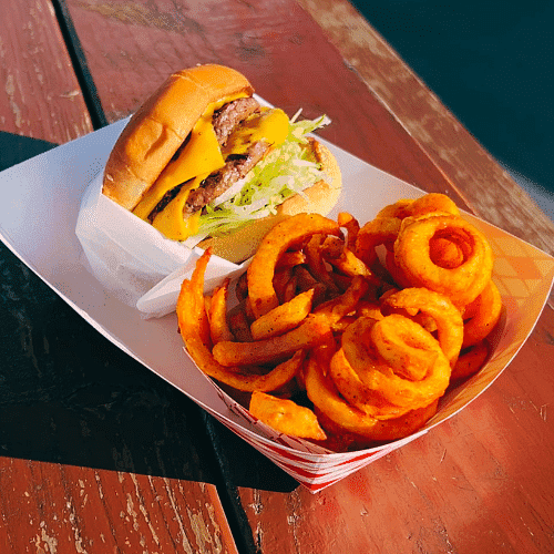Beef burger with lettuce and curly fries on a tray outdoor.
