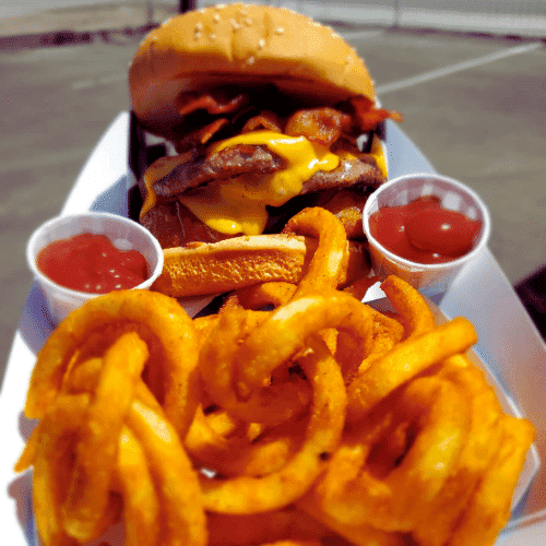 Cheeseburger with bacon, curly fries, and condiments on a plate.
