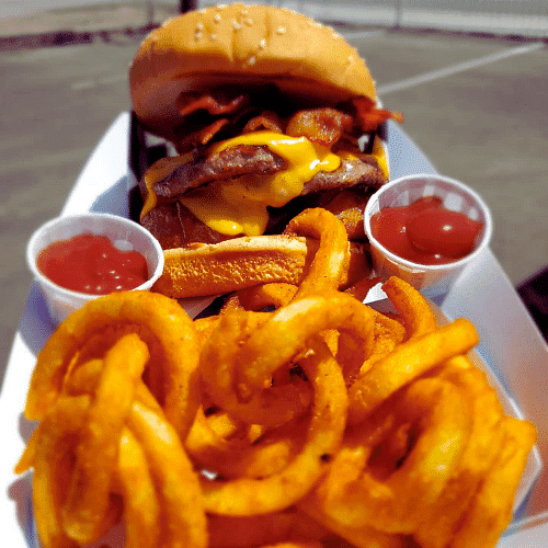 Cheeseburger with bacon, curly fries, and condiments on a plate.