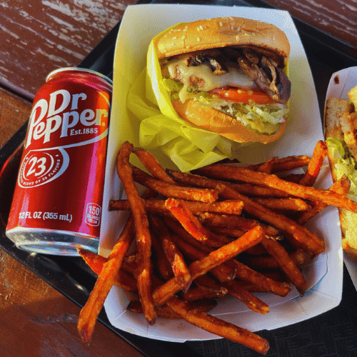 A burger with sides of sweet potato fries and a can of Dr Pepper.